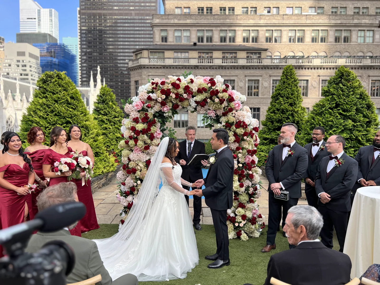 A bride and groom exchange vows beneath a floral arch at their rooftop wedding ceremony.