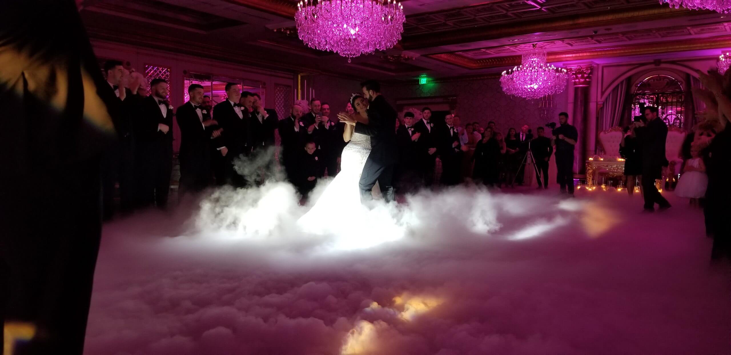 A couple shares a first dance surrounded by a dancing-on-clouds effect as their guests look on.