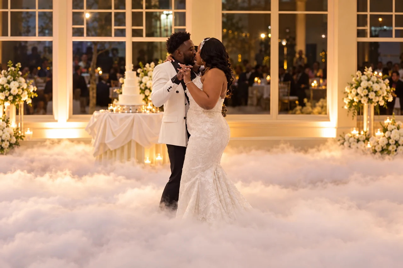 A couple shares a first dance surrounded by a dancing-on-clouds effect as their guests look on.
